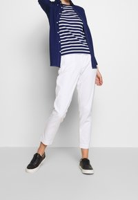 Granatowa koszula z guzikami noszona na paskowanej granatowo-białej koszulce, w zestawieniu z białymi spodami 3/4 i czarnymi trampkami. Prosty, casualowy strój.