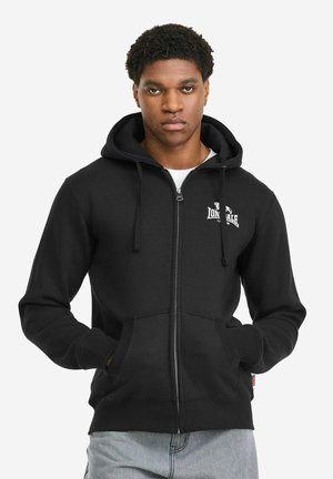 Črna kapa z zadrgo iz mešanice bombaža, z žepom kenguru in kapuco z vrvico. Na prsih je natisnjen logotip, z rebrastimi manšetami in spodnjim robom.