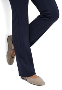 Grijze suède ballerina's met een ronde neus en een elastische band, gecombineerd met donkerblauwe broek met een nette, op maat gemaakte uitstraling.