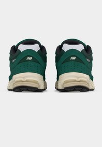 Ζευγάρι αθλητικών παπουτσιών New Balance 2002R σε πράσινο και άσπρο, εμφανιζόμενα από πίσω με μαύρες σόλες και λεπτομέρεια διάτρητης φτέρνας.