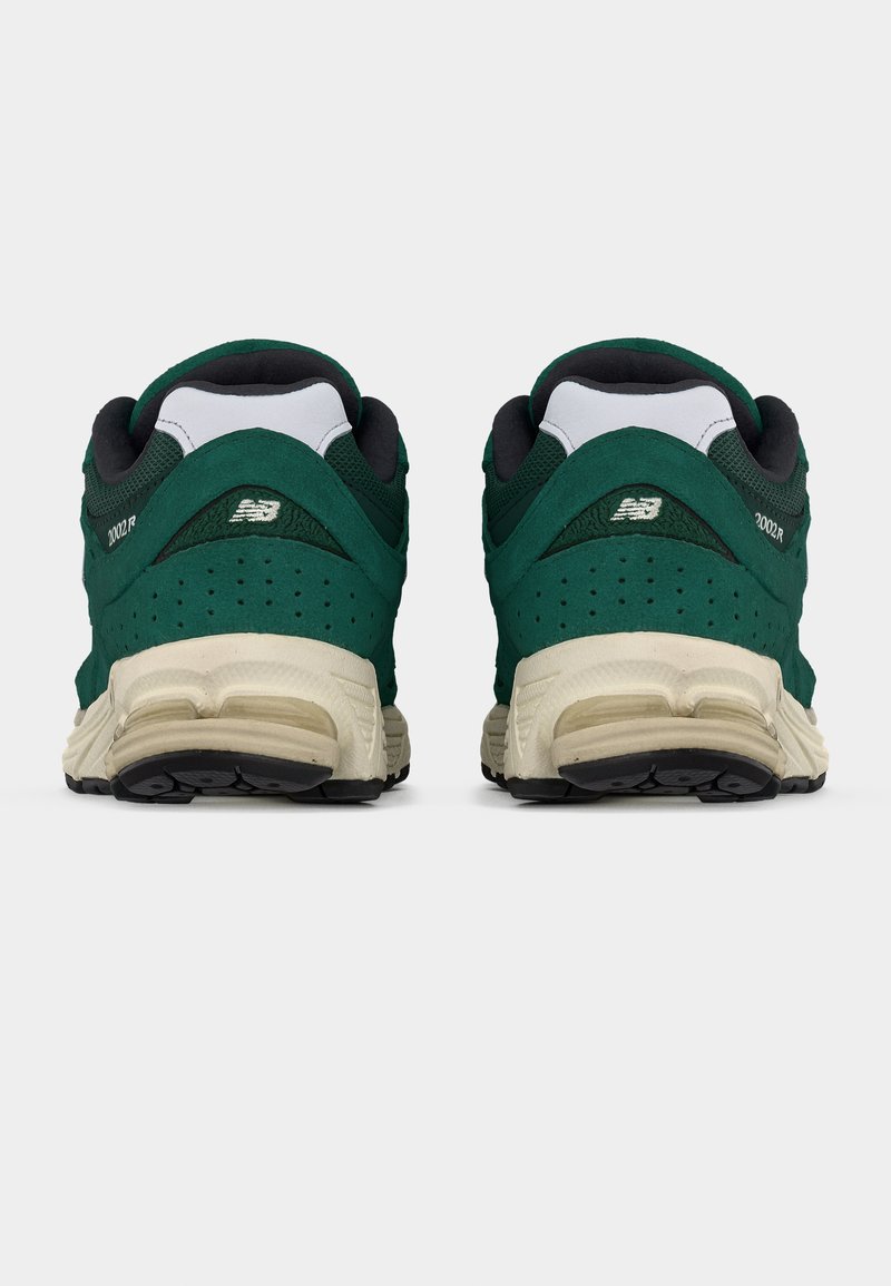 Paire de baskets New Balance 2002R vertes et blanches vues de dos avec semelles noires et détail perforé sur le talon.