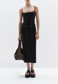 Black sleeveless dress with a square neckline, fitted design, and knee-length, paired with a brown suede handbag and black platform sandals.