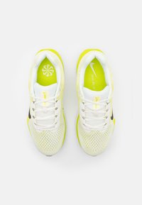 Baskets de course blanches et jaune vif avec une tige en mesh, un logo Nike noir, des lacets blancs et une semelle texturée. Design de logo intérieur accentué.