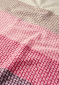 Couverture tissée avec un motif à carreaux dans des tons de rose, beige clair et violet, avec une surface douce et texturée.