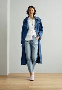 Denim långjacka i mörkblått, vit skjorta, ljusblå jeans och blekrosa skor. Har klassisk krage och avslappnad passform. Träddäck som bakgrund.