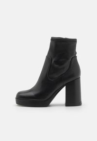 Botines de cuero negro con puntera redondeada, paneles laterales elásticos y un tacón grueso. Textura suave con acentos de costura mínima.