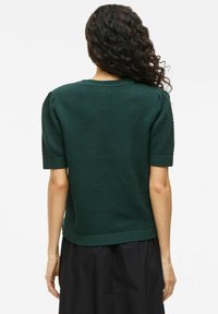 Suéter verde de punto con mangas cortas, patrón texturizado de panal y dobladillo acanalado. Estilo ajustado con cuello redondo, mostrado desde la parte posterior.