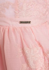 Różowa sukienka z tkaniny, zdobiona haftem kwiatowym na dole, o fałdowanej fakturze oraz metalową metką z nazwą "Marciano."