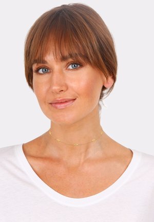 Gold choker necklace featuring geometric diamond-shaped accents, delicate links, and a simple design, worn with a white V-neck shirt.