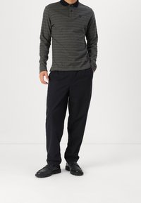 Langärmeliges, grau gestreiftes Polo mit schwarzem Kragen, kombiniert mit weit geschnittenen schwarzen Hosen und schwarzen Schuhen, mit entspanntem Sitz.