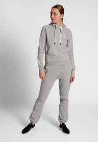 Grijze hoodie en bijpassende sweatpants van zachte stof, met een voorzak, trekkoord en manchetten aan de enkels. Zwarte sportschoenen.