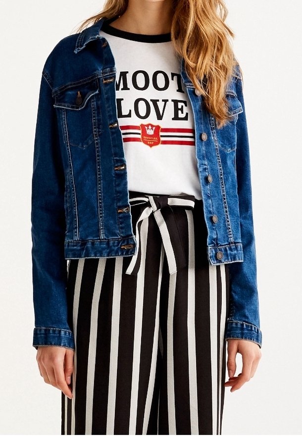 Femme portant une veste en jean bleue, un t-shirt blanc graphique avec le texte "MOOT LOVE", et un pantalon taille haute à rayures verticales noires et blanches avec une ceinture nouée.
