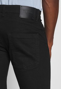 Mustat farkut sisältävät nahkavyötaskun, jossa on kohokuvioitu teksti, takataskun hienovarainen tikkaus ja slim fit -muotoilu.
