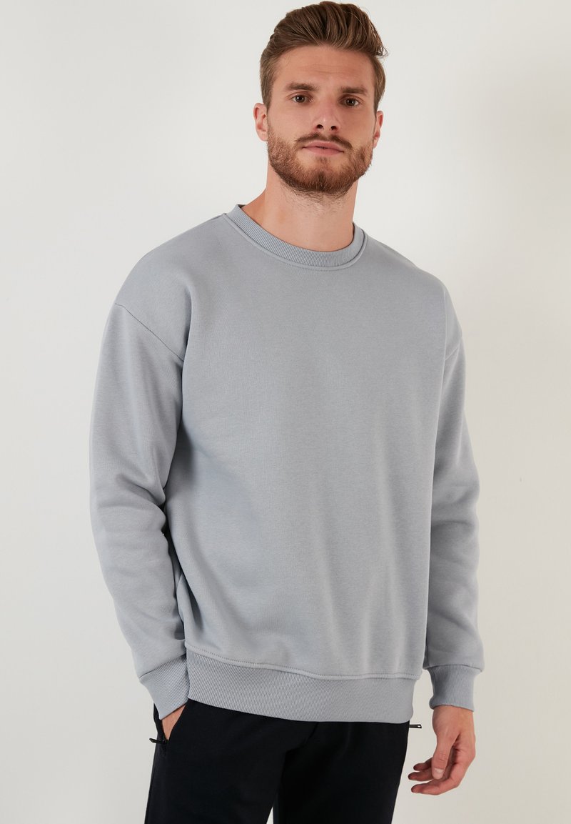 Sudadera gris claro con cuello redondo, puños y dobladillo de canalé. Fabricada en tejido suave, presenta un corte relajado y un diseño de hombros sin costuras.