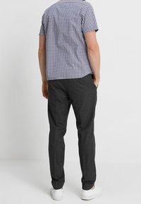Camicia a maniche corte a quadri blu navy e bianca, abbinata a pantaloni grigi scuri. Entrambi i capi presentano una vestibilità rilassata e sneakers bianche semplici.