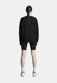Fekete pulóver laza fazonnal, fekete bicikliz shorts-al párosítva. Figyelemre méltó részletek közé tartozik a textúrált anyag és a fehér sportcipők.