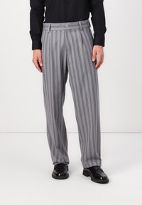 Striped gray trousers with a wide-leg design, featuring a button closure and pleats. Worn with black shoes and a long-sleeve black shirt.