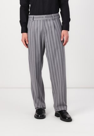 Striped gray trousers with a wide-leg design, featuring a button closure and pleats. Worn with black shoes and a long-sleeve black shirt.