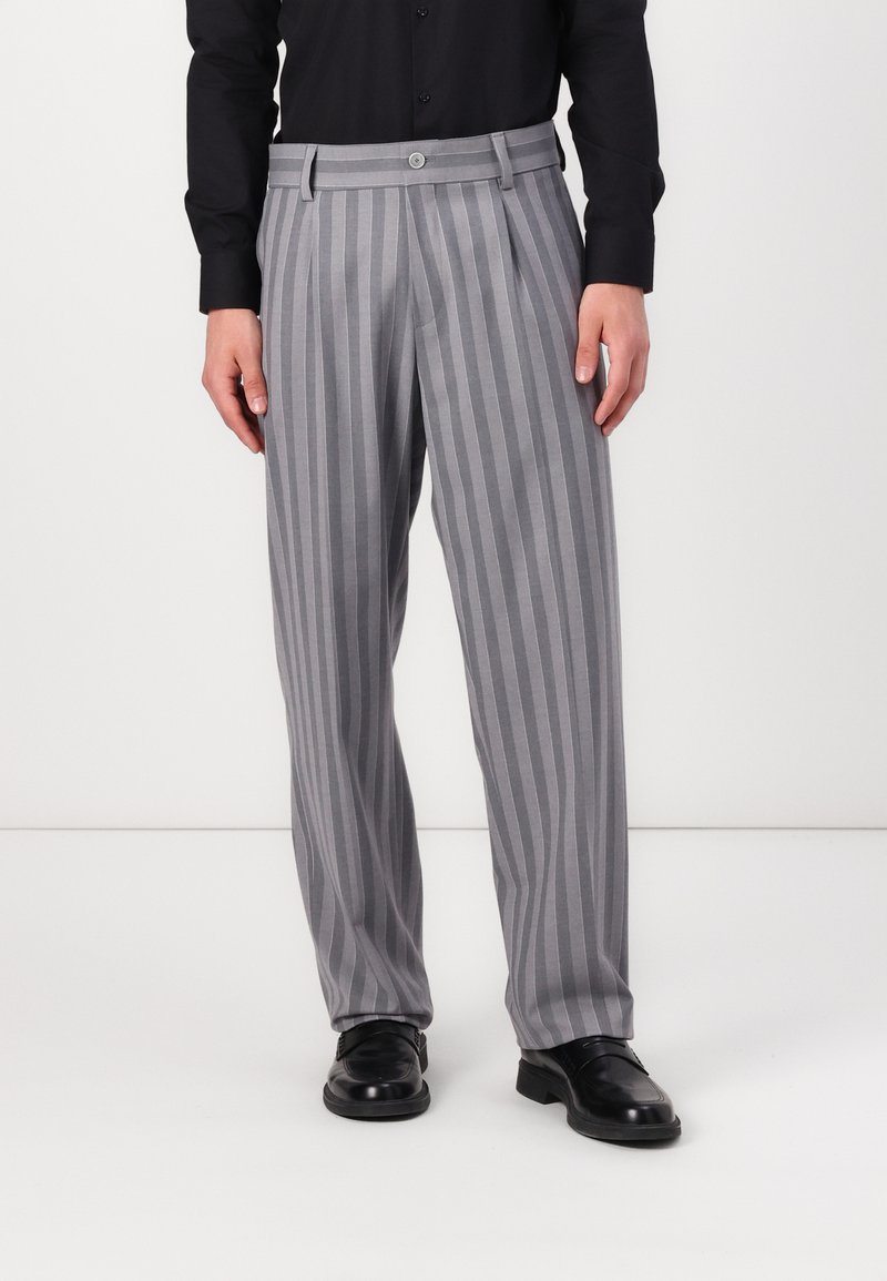 Striped gray trousers with a wide-leg design, featuring a button closure and pleats. Worn with black shoes and a long-sleeve black shirt.
