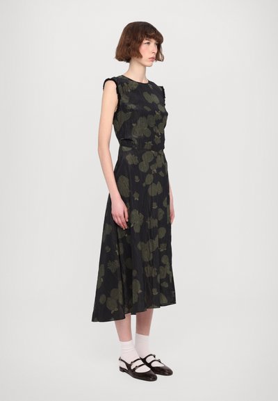 Zwarte jurk met groen bloemenpatroon, mouwloos ontwerp, gestructureerde stof, halflange rok, gecombineerd met witte sokken en donkere schoenen.