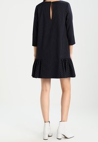 Navyblau gestreiftes Kleid mit Dreiviertelärmeln, rüschenbesetztem Saum und einem Schlüssellochverschluss hinten. Kombiniert mit weißen Ankle Boots.