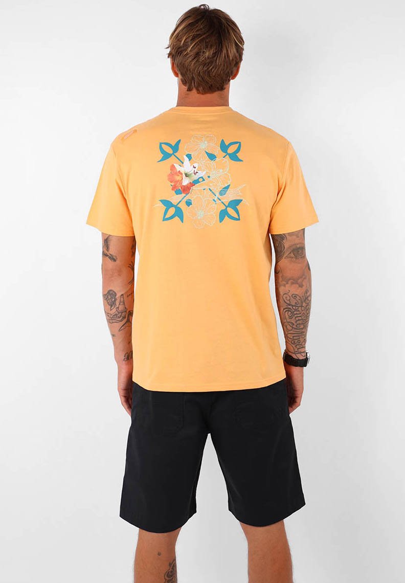 T-shirt en coton jaune affichant un graphique floral et de feuilles en bleu et orange au dos. Manches courtes et coupe décontractée. Shorts noirs portés.