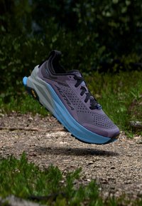 Zapatilla de correr morada con parte superior de malla transpirable, entresuela azul y suela exterior negra. Agujeros de ventilación y logo en el lateral.