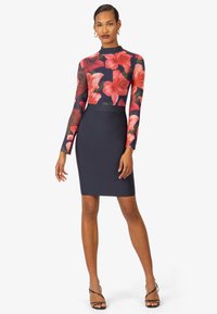 Top a maniche lunghe floreale con uno sfondo blu scuro; abbinato a una gonna a matita blu fitted. Presenta maniche trasparenti e una texture liscia.