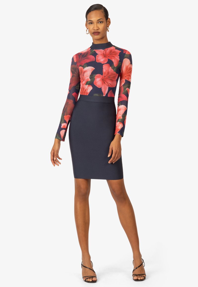 Top a maniche lunghe floreale con uno sfondo blu scuro; abbinato a una gonna a matita blu fitted. Presenta maniche trasparenti e una texture liscia.