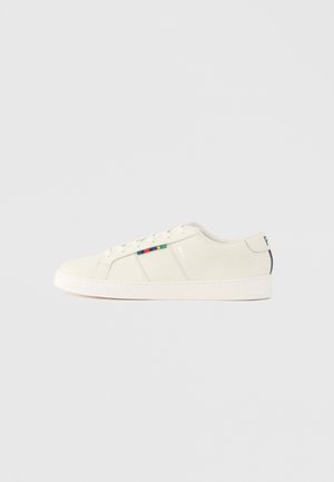 Ténis bege claro com textura suave, design de atacadores e detalhe listrado colorido na lateral. Sola de borracha branca. Parte de trás lisa.