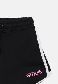 Μαύρο σορτς από βαμβακερό μείγμα με υφή, με ροζ λογότυπο "GUESS" και λευκές πλευρικές ρίγες. Ελαστική μέση με κορδόνι.