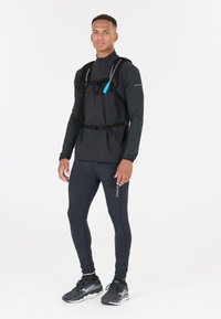 Black lightweight athletic top with a zip and straps, paired with black fitted leggings and matching running shoes. Accented with blue hardware.