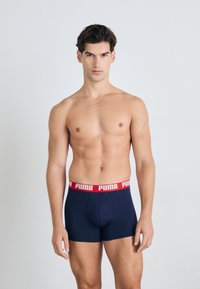 Boxeri scurți dintr-un material elastic albastru, cu o bandă roșie la talie, pe care se află un logo alb "PUMA". Au o textură netedă și un design ajustat, prezentate pe un model.