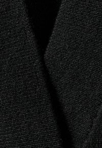 Čierna pletená tkanina s textúrovaným povrchom, s výrazným dizajnom vo forme písmena V a viditeľnými vláknami priadze, čo vytvára jemný vzhľad.