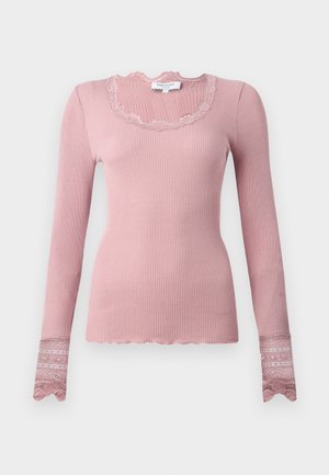 Langsleeve ribbeltop in zachtroze met een geschulpte halslijn en kanten manchetten die ingewikkelde patronen tonen. Gemaakt van rekbaar materiaal.