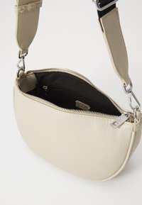 Beige leather crossbody bag with a textured exterior, zip closure, and an interior pocket. Features silver hardware and an adjustable strap.