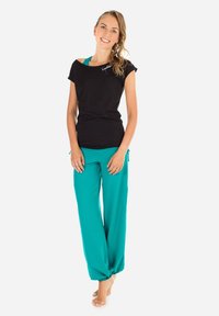 Black short-sleeve shirt with a relaxed neckline, paired with loose, teal pants featuring elastic cuffs and side ties.