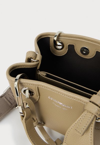 Μπεζ δερμάτινη γυναικεία τσάντα χειρός με ασημένια μεταλλικά στοιχεία, δύο λαβές και μαύρο εσωτερικό. Διαθέτει υφή στην επιφάνεια και διπλά διαμερίσματα.