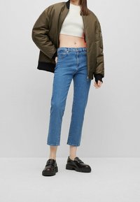 Olivgrön bomberjacka, cropped vit topp, högmidjade blå denimjeans och svarta chunky loafers med strukturerade sulor.