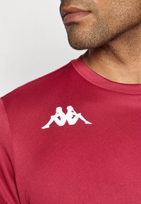 Rode sportshirt met een ronde halslijn en een opvallend wit logo op de borst, ontworpen voor comfort en prestaties.