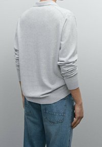 Szara bluza z prążkowanymi mankietami i kołnierzem, o luźnym kroju. Połączona z jasnoniebieskimi dżinsami. Prosty design, bez widocznych wzorów.