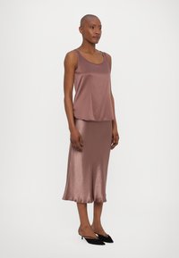 Satin two-piece outfit in muted mauve, featuring a sleeveless top and a flowing, knee-length skirt with a subtle sheen. Black shoes.