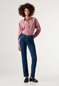 Κόκκινο και λευκό ριγέ πουκάμισο με κουμπιά και μακριά μανίκια, συνδυασμένο με μπλε τζιν παντελόνι και μαύρα μοκασίνια. Λείο ύφασμα, κλασική εφαρμογή.