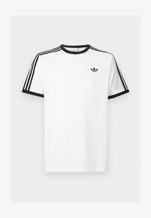 Balts kokvilnas t-kreklis ar melnu ribotu kaklu un piedurknēm, kuram uz katra pleca ir trīs melnas svītras un neliels logo krūtīs.