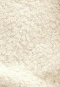 Tissu texturé ivoire avec des boucles douces et en relief, ressemblant à de la polaire, créant une apparence moelleuse et confortable.