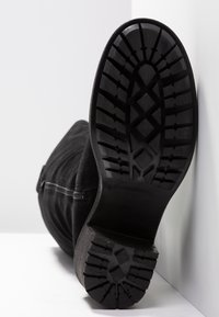 Bottine noire en daim avec une semelle en caoutchouc côtelée présentant un motif en zigzag. Détail zippé sur le côté, bout rond et talon légèrement surélevé.