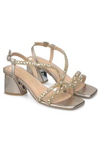 Metallic gold strappy sandals featuring embellished straps, square toes, and a chunky mid-heel. Smooth texture with a sleek finish.