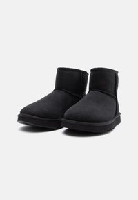 Musta nilkkuri suede-materiaalista, jossa on pyöreä kärki ja paksut, litteät kumipohjat. Varressa on ommeltuja yksityiskohtia.