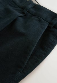 Dunkelblaue Stoffhosen mit einer glatten Textur, die einen Bund und Falten an der Vorderseite für ein strukturiertes Design aufweisen.
