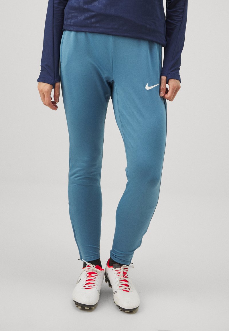 Hellblaue Sporthosen mit schmaler Passform. Mit einem weißen Nike-Logo auf dem Oberschenkel. Getragen mit weißen Fußballschuhen und roten Akzenten.